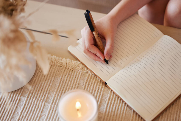 Hand, candle and woman writing in journal with top view for calm, peace mindset and relax morning routine in home. Hands, notebook and diary planning goals, idea vision or creative writer lifestyle. - Foto, imagen