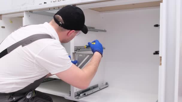 Ένας επαγγελματίας τεχνίτης εγκαθιστά έπιπλα στην κουζίνα χρησιμοποιώντας ένα κατσαβίδι. Θέση συρταριών στα κομοδίνα. Σχέδιο ανακαίνισης σπιτιού - Πλάνα, βίντεο