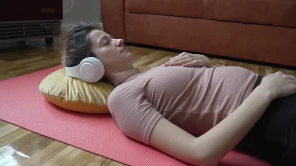 オンラインガイド付き瞑想のためのヘッドフォンを使用して1人の女性大人の白人女性千年紀自宅で床に目を閉じてマインドフルネスヨガを練習本当の人々のセルフケアの概念 - 映像、動画
