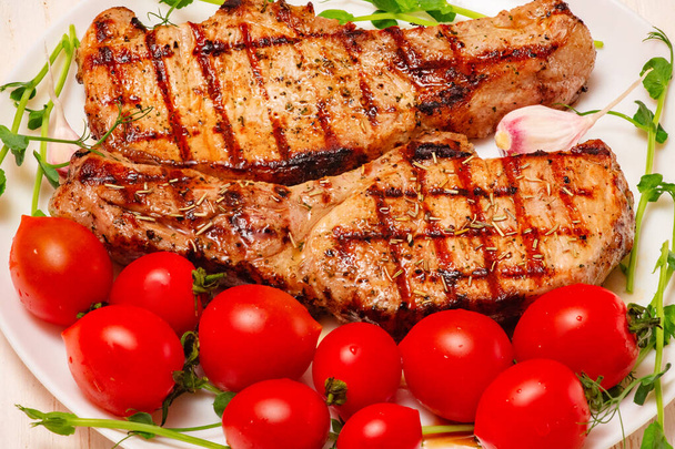 Meat with herbs, garlic and tomatoes. Two fried steaks in a plate with tomatoes. - Foto, Imagem