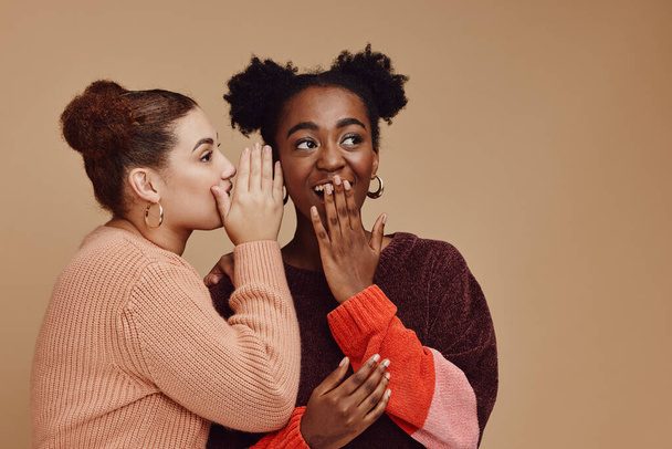 Friends, gossip and women share secret on studio background and product placement mockup. Secrets, rumor and surprise whisper in ear, black woman with happy woman discuss discount sale announcement. - Valokuva, kuva