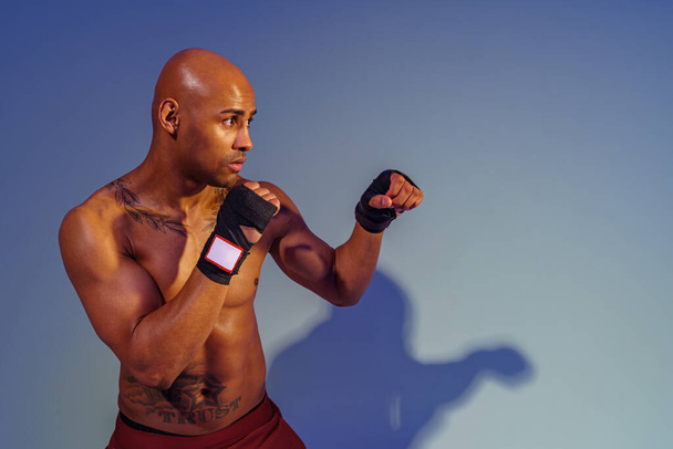 Professional kickboxer is training and practicing punch on studio background with color filter - Фото, зображення