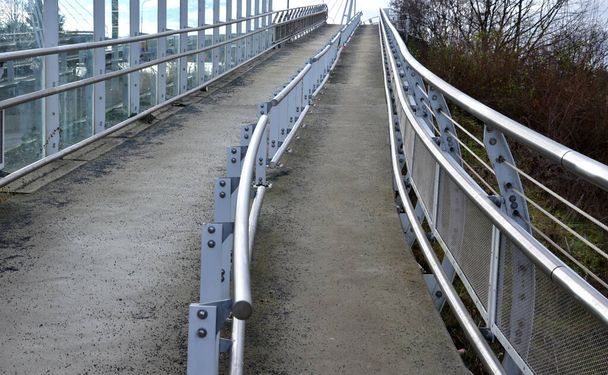 歩道橋は傾斜が長い傾斜路で、ステンレス製の手すりが車椅子や歩行者用に部分を分けています。車椅子の方が丘を登れなくなったら手すりにつかまって  - 写真・画像