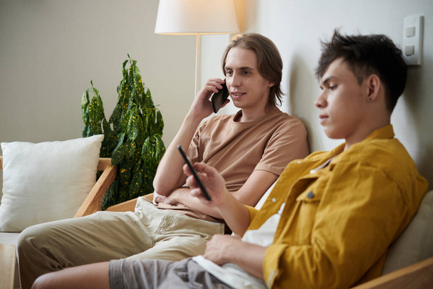 Молодий чоловік розмовляє по телефону, коли його друг пише або перевіряє соціальні медіа
 - Фото, зображення