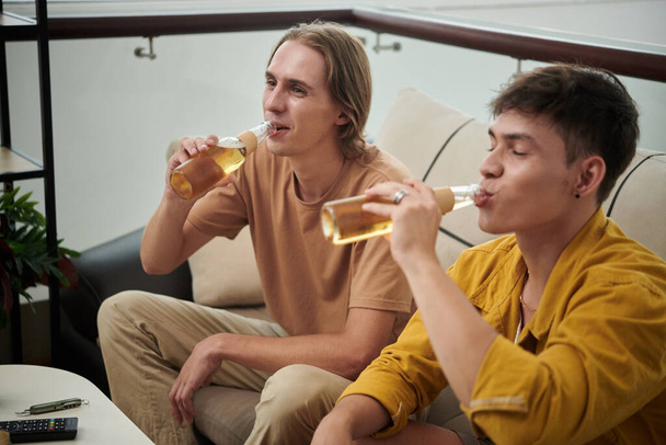 Young man drinking bottled beer when watching movie or soccer game at home - Foto, Imagem