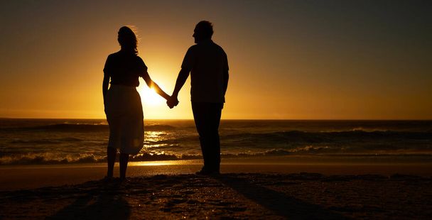 Силуэт зрелой пары, держащейся за руки на пляже на закате. Старшая пара вместе отдыхает. Зрелая пара, любящая отдых на пляже. Пожилая пара на берегу моря vacatio. - Фото, изображение