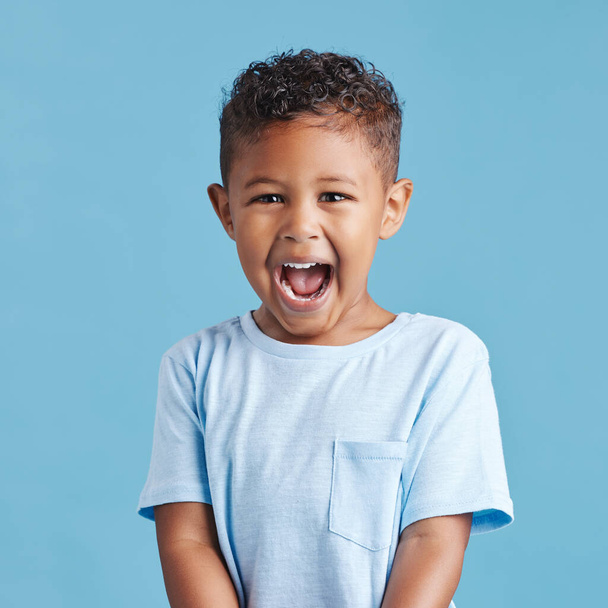 Close up of excited little boy looking happy and shouting while standing against a blue studio background. Cute preschooler wearing casual clothes. - Foto, Imagen