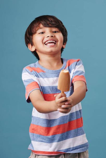Portrait of an adorable little asian boy looking happy while enjoying a sweet treat against a blue background. Mixed race child eating a sugar dipped popsicle as a snack. - Fotoğraf, Görsel