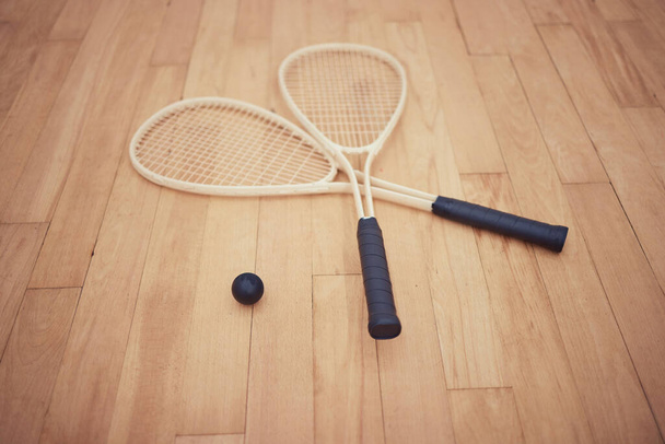 Group of squash equipment and gear on wooden floor in empty court in sports centre with copyspace. Two rackets and ball arranged in sporty arena with nobody before championship game and competition. - Photo, image