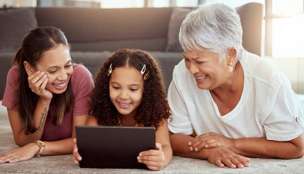 Adorable little mixed race child bonding with single mother and grandmother and using digital tablet at home. Parent and senior woman lying on living room floor together with kid and using technology. - Fotoğraf, Görsel