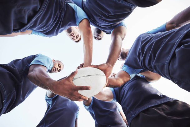 Poniżej zróżnicowana grupa graczy rugby stojących w zgrupowaniu razem na zewnątrz na boisku. Młodzi męscy sportowcy wyglądający poważnie i skupieni podczas zbiórki jako drużyna. Gotowy na trudne gry. - Zdjęcie, obraz