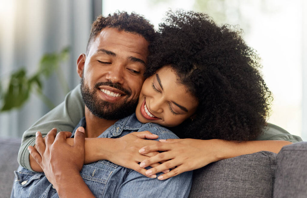 Young happy mixed race couple embracing while relaxing at home. Hispanic boyfriend and girlfriend smiling while hugging in the lounge at home. - Foto, Imagem