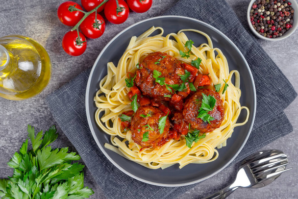 Homemade spaghetti with tomato sauce meatballs and spices served in black plate on gray concrete background. Tasty cooked pasta with minced beef meat balls and food ingredients. Top View, Flat lay. - Foto, Imagen