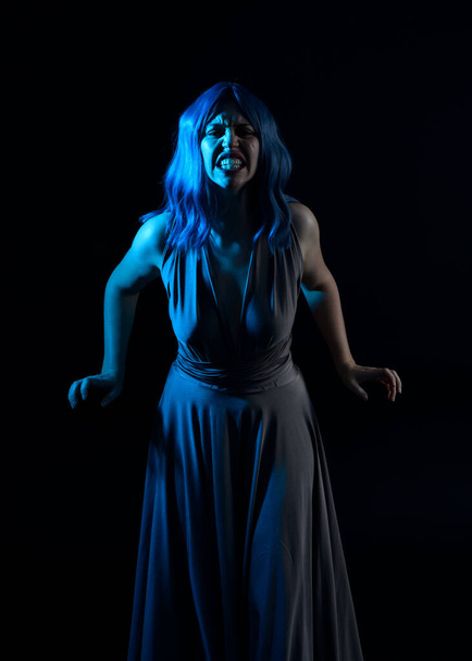 πορτρέτο του όμορφου κοριτσιού με μπλε περούκα μαλλιών & κομψό φόρεμα με εκφραστικές εκφράσεις προσώπου & χειρονομίες βραχίονα θέτει. πολύχρωμος φωτισμός νέον τζελ, απομονωμένος σε φόντο στούντιο. - Φωτογραφία, εικόνα