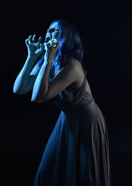 portrait of pretty girl with blue hair wig & elegant gown with expressive facial expressions & gestural arm poses. colourful neon gel lighting, isolated on studio background. - Foto, afbeelding