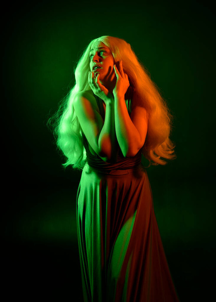 portrait of pretty girl with blonde hair & elegant gown with expressive facial expressions & gestural arm poses. colourful neon gel lighting, isolated on black studio background. - Photo, Image