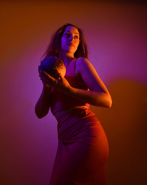 Low angle portrait of pretty girl wearing pink outfit, gestural arm poses reaching out as if casting a spell, colourful neon gel lighting, isolated on studio background. - Foto, immagini