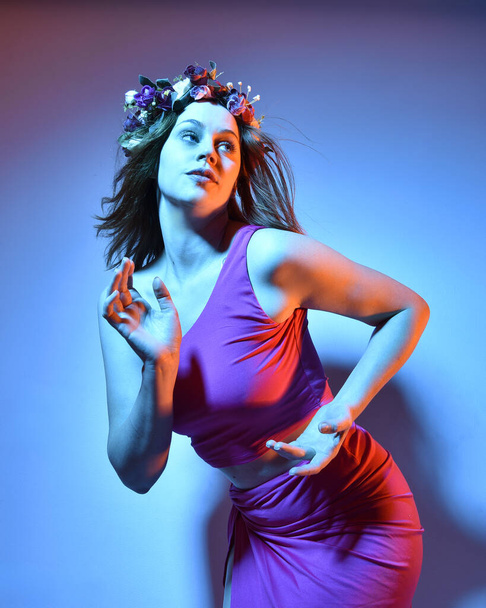 Low angle portrait of pretty girl wearing pink outfit, gestural arm poses reaching out as if casting a spell, colourful neon gel lighting, isolated on studio background. - Foto, immagini