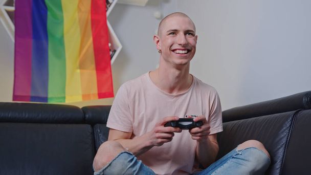 Χαμογελώντας queer άνθρωπος που παίζει βιντεοπαιχνίδια με ένα consol εσωτερική. Υψηλής ποιότητας φωτογραφία - Φωτογραφία, εικόνα