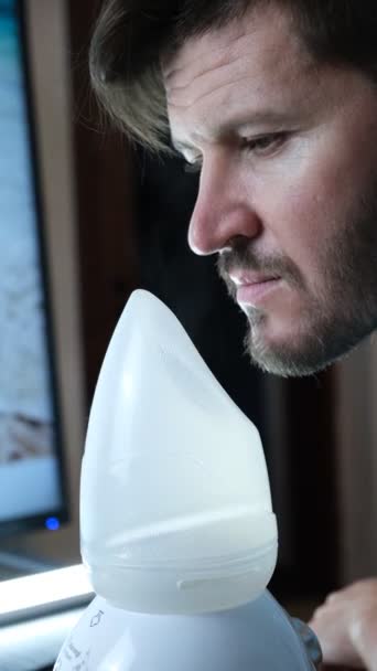 An adult man breathes steam, treats the airways with a nebulizer at home. The guy is sitting with an inhaler, a treatment for bronchitis, covid, a Nebulizer, a handsome man. Prevention and treatment - Footage, Video