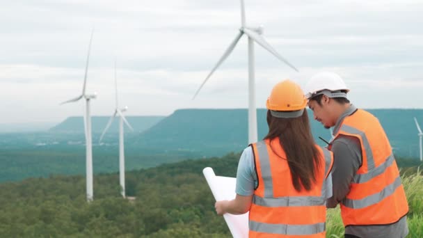 Мужчины и женщины-инженеры, работающие на ветряной электростанции на вершине холма или горы в сельской местности. Прогрессивный идеал для будущего производства возобновляемых источников энергии, устойчивой. - Кадры, видео