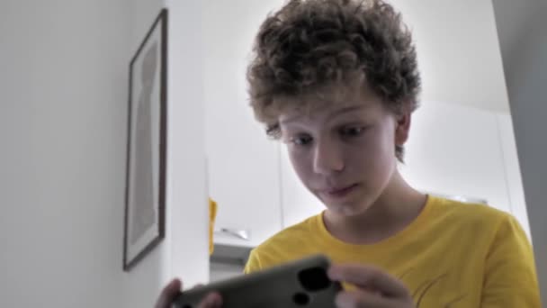 Un adolescente de pelo rizado juega juegos de ordenador en su habitación. Adicción al juego, problemas de la adolescencia - Imágenes, Vídeo