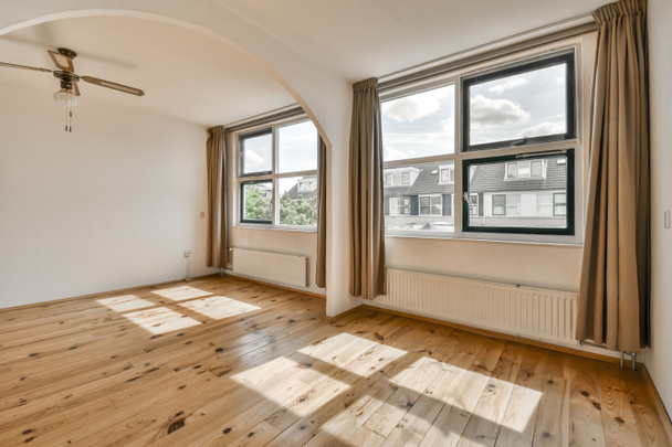 een lege woonkamer met houten vloeren en grote ramen die uitkijken op de straat voor het huis - Foto, afbeelding