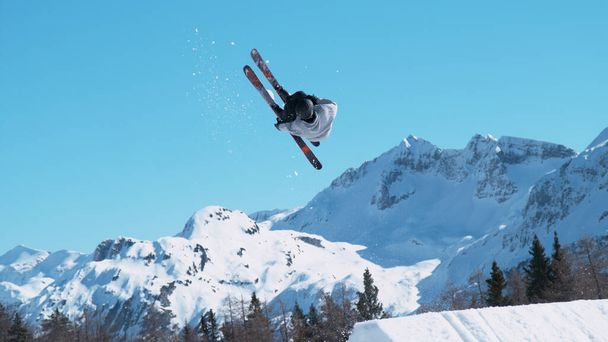 キッカーから飛び降り、美しいバックフリップを行う極端なスキーヤーの壮大なショット。日本の山の中でフリースタイルのスキーは晴れた冬の日に裏技を行います. - 写真・画像