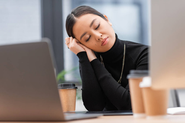 Сонний азіатський дизайнер сидить біля комп'ютерів і кави в офісі
  - Фото, зображення