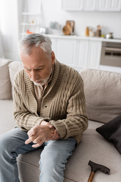 αγχωμένος άνθρωπος με νόσο Parkinson και τρέμουλο στα χέρια κάθεται στον καναπέ στο σπίτι - Φωτογραφία, εικόνα