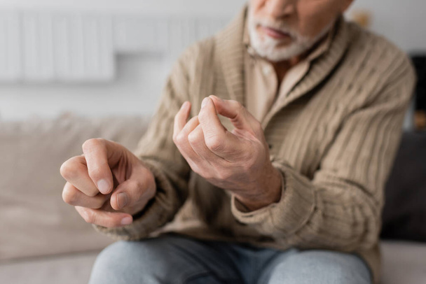 partial view of aged man with parkinson disease and trembling hands sitting at home - Foto, Imagen