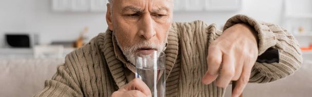 worried man with parkinsonian syndrome holding glass of water in trembling hand, banner - Photo, Image