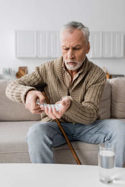 aged man with parkinson syndrome holding pills in trembling hands while sitting on couch at home - Zdjęcie, obraz