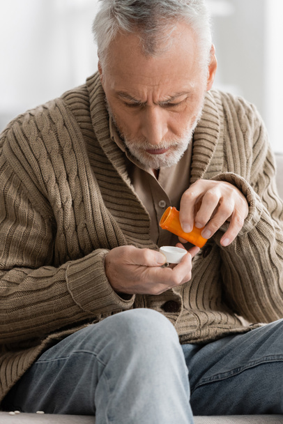 grey haired man in knitted cardigan holding pills from parkinson disease in trembling hands - Foto, afbeelding