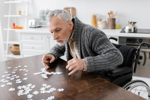 man with disability and parkinson syndrome sitting near jigsaw puzzle on table at home - Photo, Image