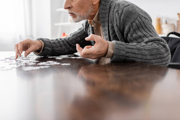 cropped view of man with parkinson disease and trembling hands sitting near jigsaw puzzle at home - Zdjęcie, obraz