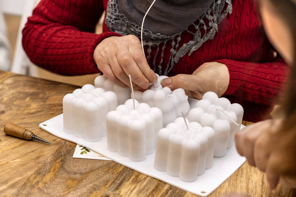 Elderly woman works silicone molds to make soy candles. Handmade soy wax candle workshop. - Photo, Image