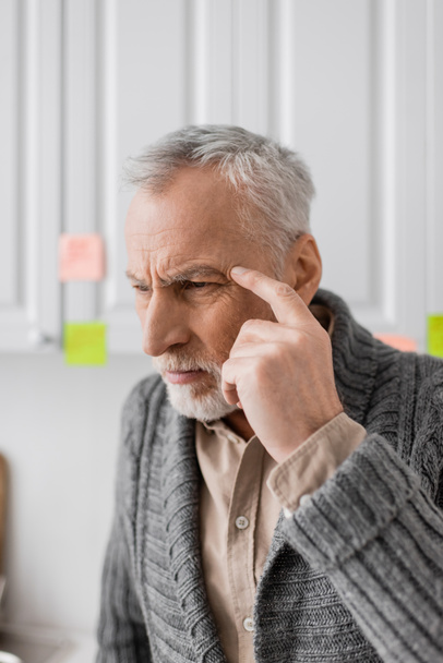 tensed man suffering from memory loss and touching head while thinking near blurred sticky notes in kitchen - Photo, Image