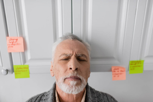 depressed man suffering from azheimers syndrome standing with closed eyes in kitchen - Photo, Image