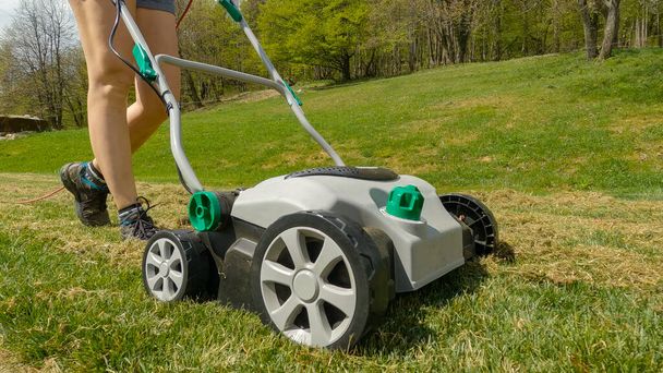 CLOSE UP: Female gardener using lawn aerator to grow healthier and thicker lawn. Spring backyard garden work for lawn growth enhancement. Practical gardening machinery for efficiency at landscaping. - Photo, Image
