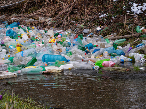 閉じる:川の端でキャッチされた様々なプラスチックボトルの蓄積された山。捨てられたプラスチックごみと汚染された川の心配ビュー。川面に浮かぶペットボトルの集積. - 写真・画像