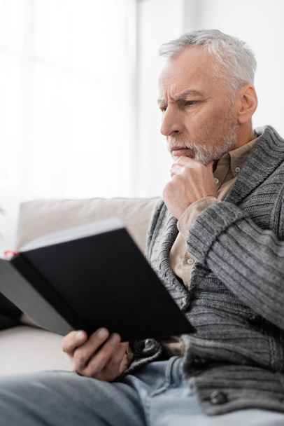 アルツハイマー病の老人が自宅でノートを持って座っている間にあごに触れる - 写真・画像