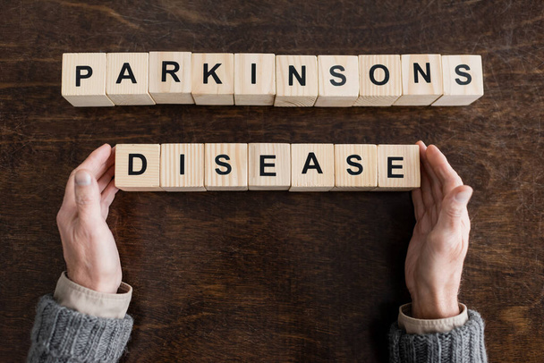 κορυφαία άποψη της περικοπεί ανώτερος άνθρωπος κοντά μπλοκ με Parkinsons ασθένεια γράμματα σε ξύλινη επιφάνεια - Φωτογραφία, εικόνα