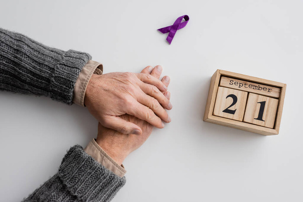 вид зверху на обрізаного чоловіка з синдромом Альцгеймера біля фіолетової стрічки та дерев'яним календарем з 21 вересня датою на білій поверхні
 - Фото, зображення