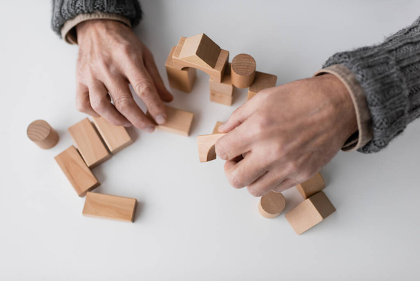 вид сверху на обрезанного человека с синдромом Альцгеймера, играющего с деревянными блоками на белом столе - Фото, изображение
