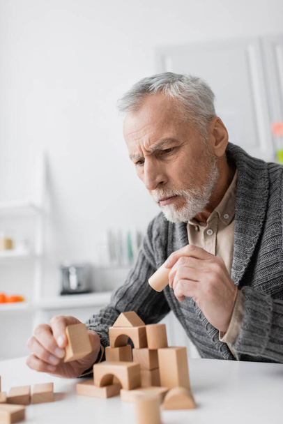 tense man with alzheimer syndrome holding wooden block while playing therapy game at home - Photo, Image