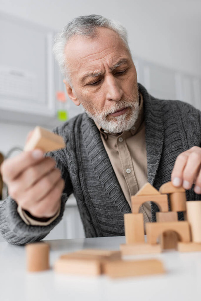 grey haired man in knitted cardigan playing building blocks game while suffering from alzheimer syndrome - Foto, Bild