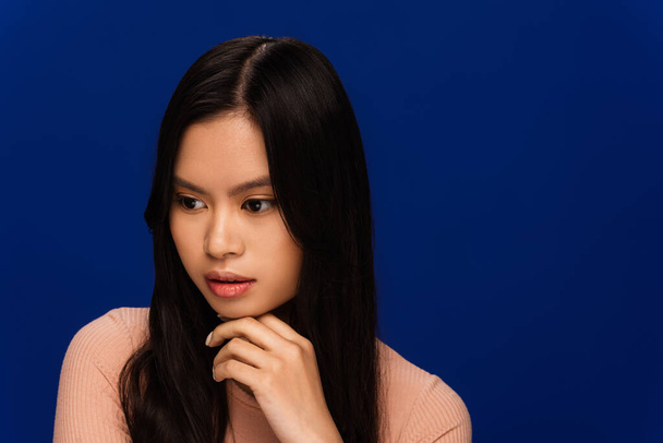 Pensive brunette asian woman looking away isolated on blue  - Fotó, kép