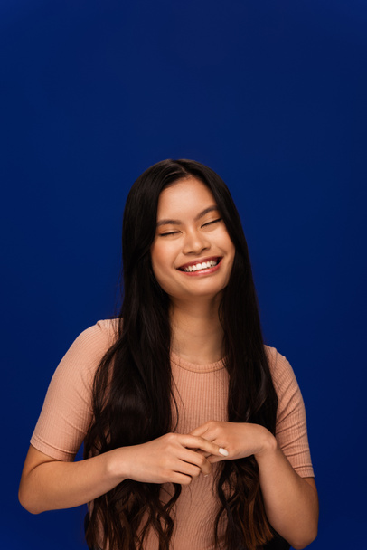 Tyytyväinen nuori aasialainen nainen beige t-paita seisoo eristetty sininen  - Valokuva, kuva