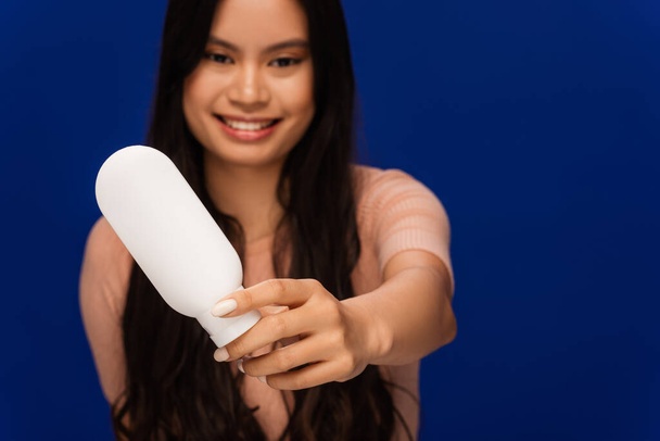 Blurred asian woman showing cosmetic lotion isolated on blue  - Fotoğraf, Görsel